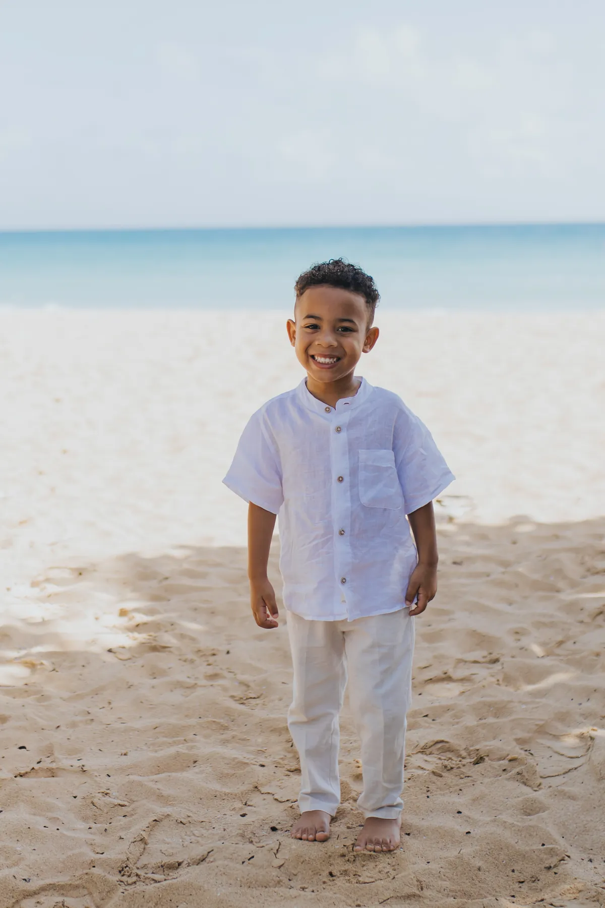 Little boy barefoot on the sand in white linen