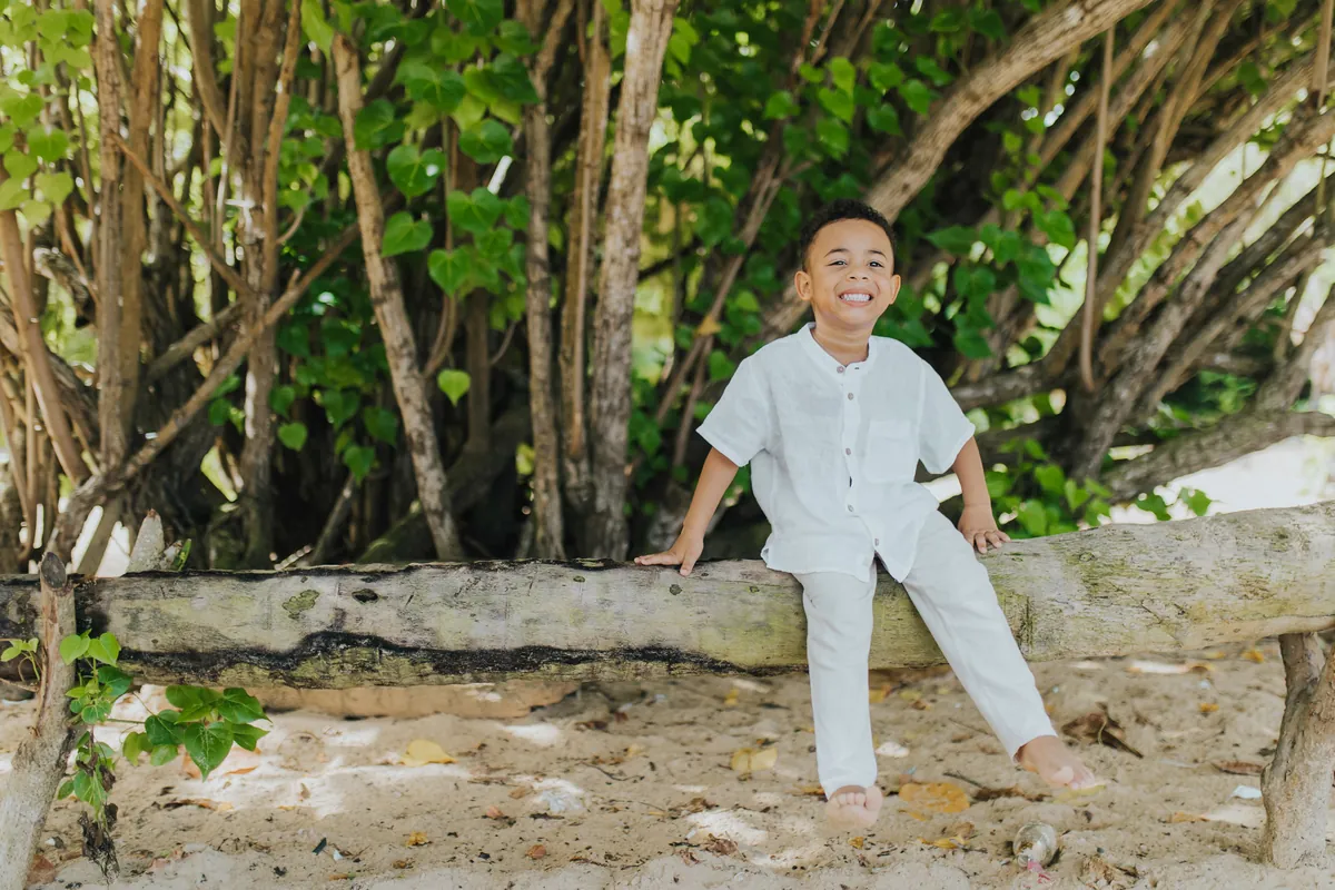 Boy grinning on a driftwood log under sea grape trees