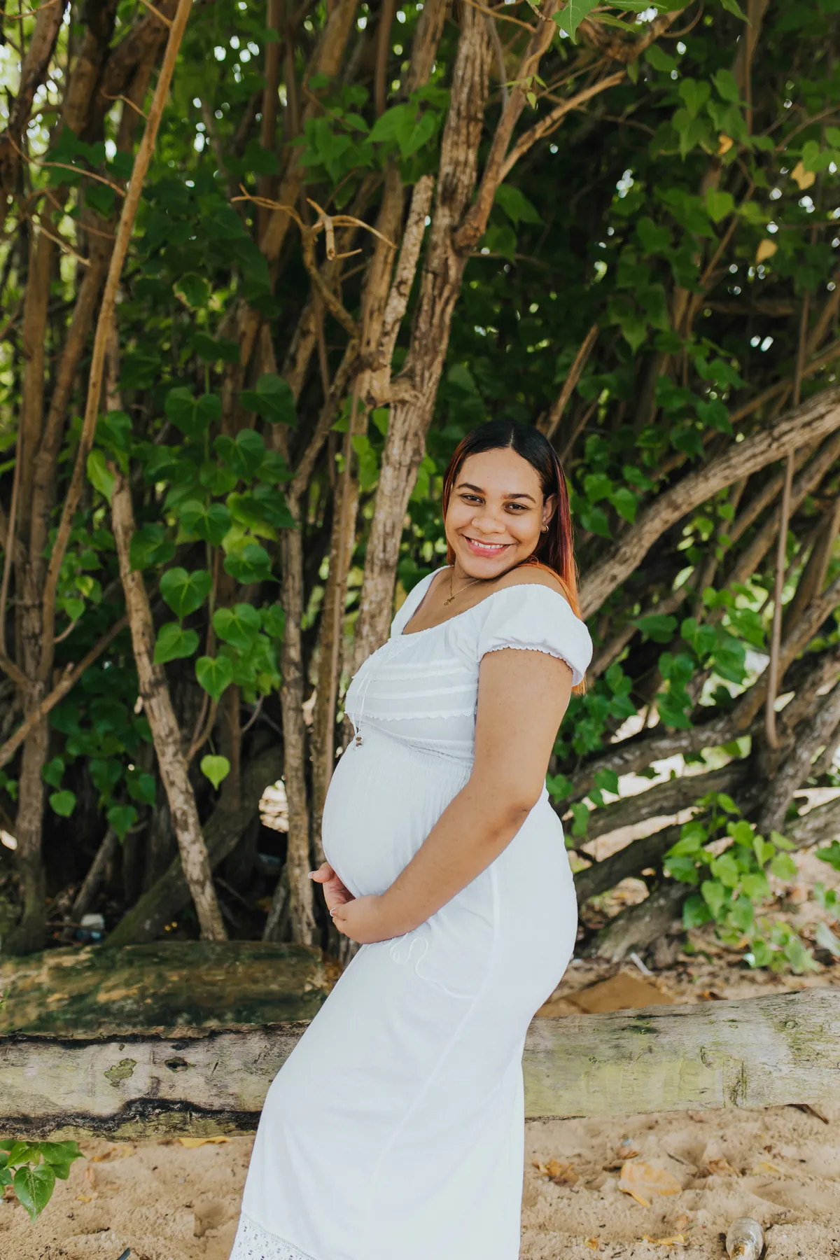 Maternity portrait in a white dress, framed by the trees