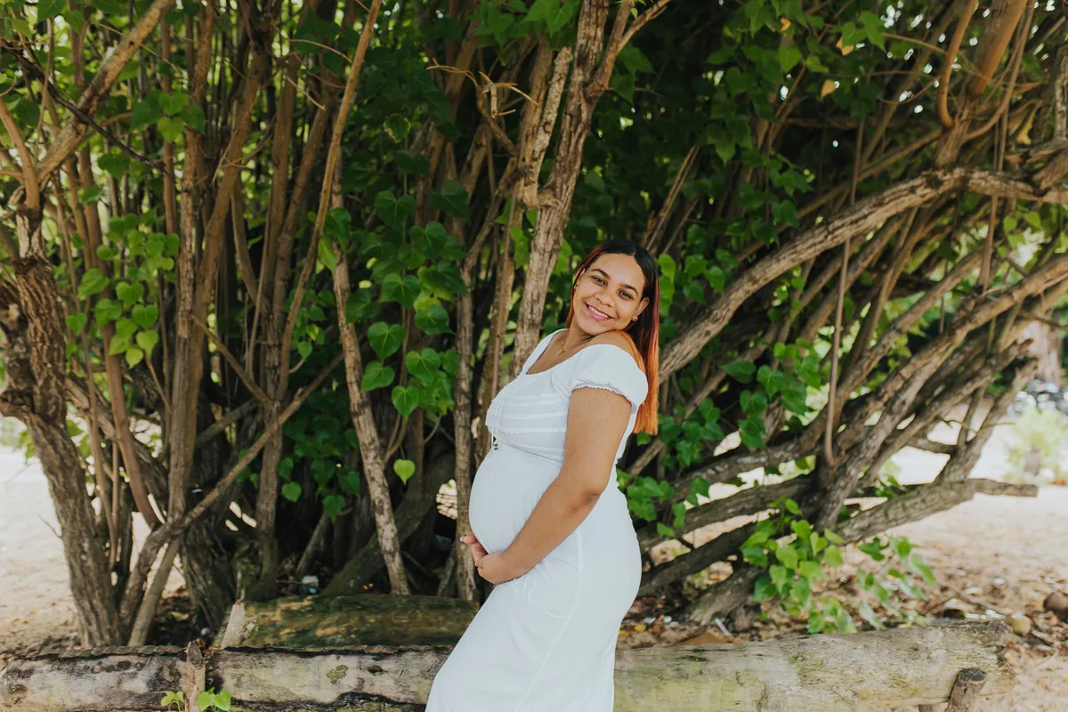 Profile of the pregnant mom holding her belly by the trees