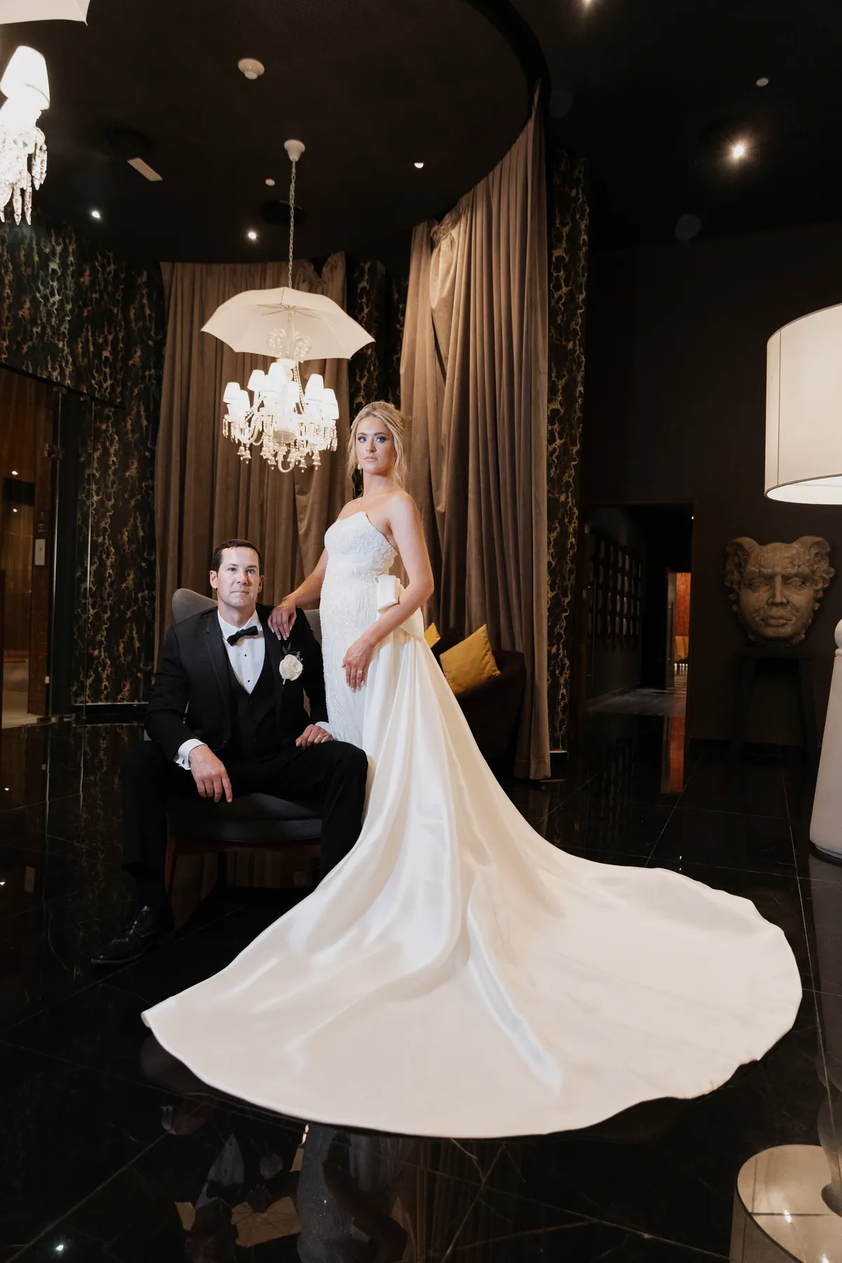 Editorial portrait of the couple under a crystal chandelier, long satin train