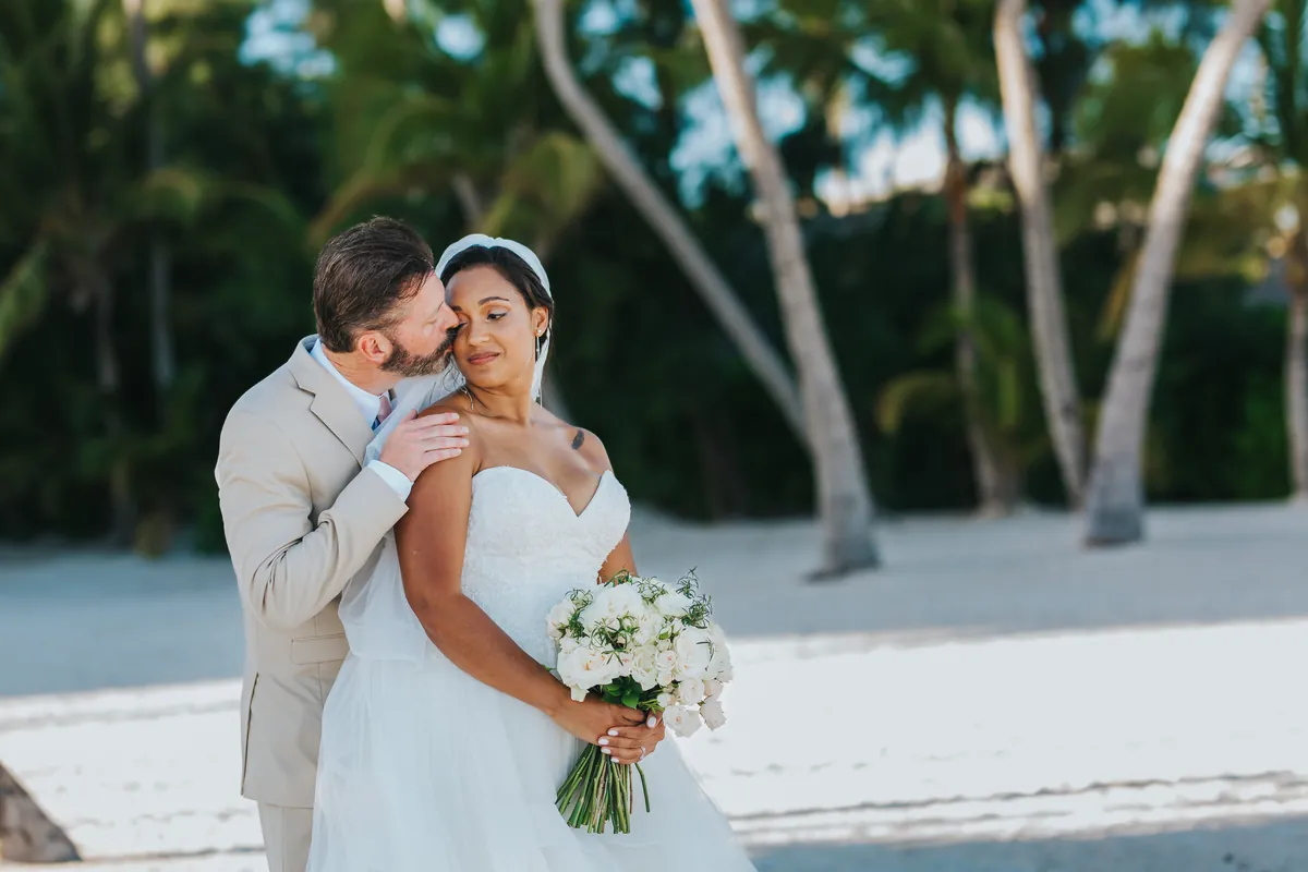 Groom kissing the bride's cheek under the palm trees