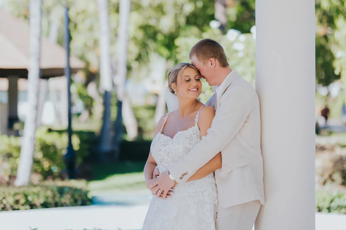 Groom hugging the smiling bride by a white column in the resort garden