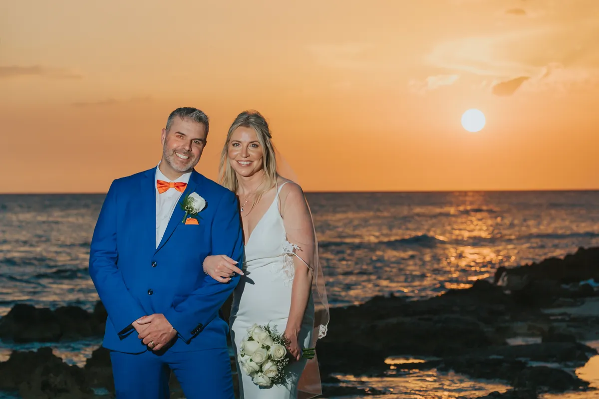 Smiling newlyweds with the sun setting over the sea