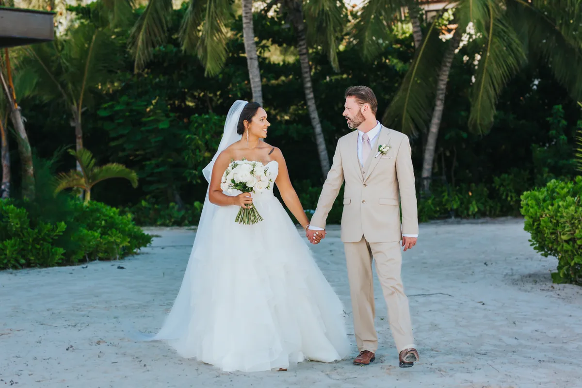 Bride and groom walking hand in hand on white sand