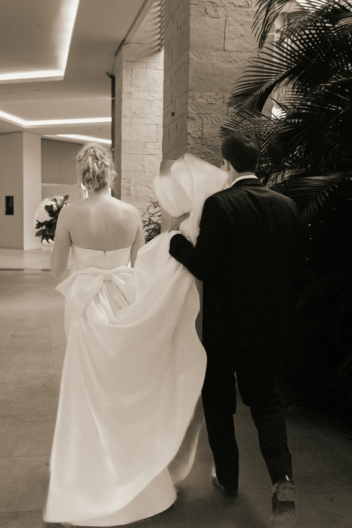The groom carrying the bride's train as they walk through the resort