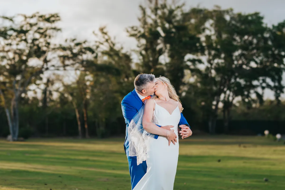 Groom kissing the bride in a green field at golden hour